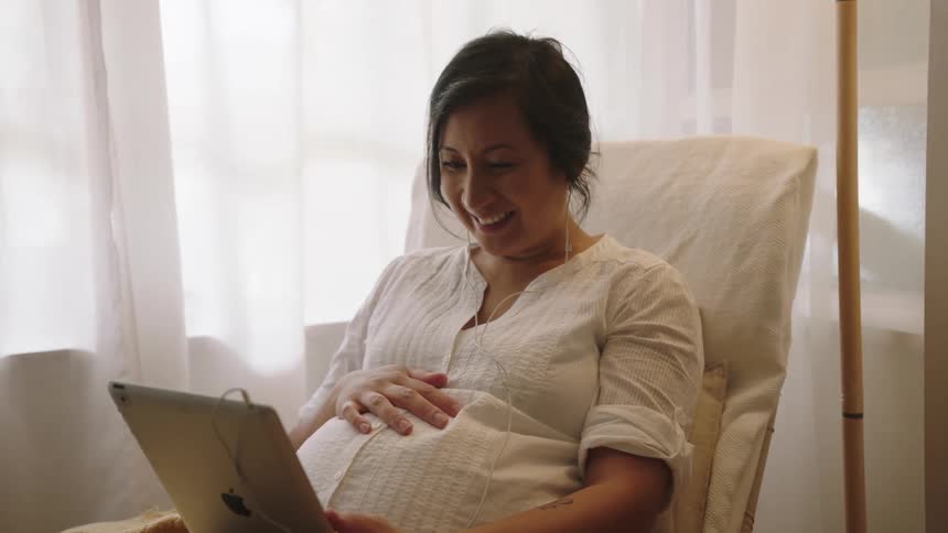A pregnant women waves and touches her stomach during a video call