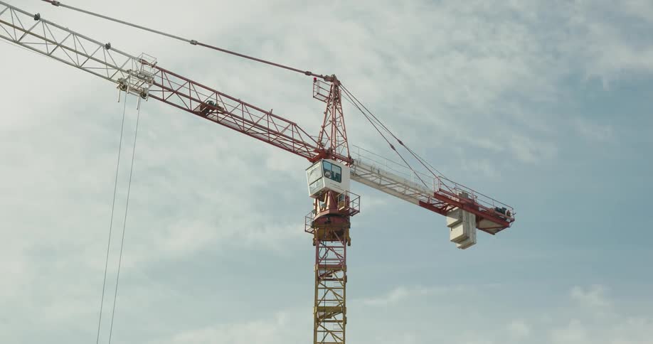 Big orange construction crane moving from right to left in front of the blue sky