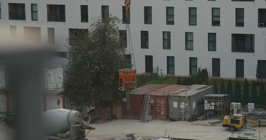 Crane lifts an orange concrete mixer container over a construction site