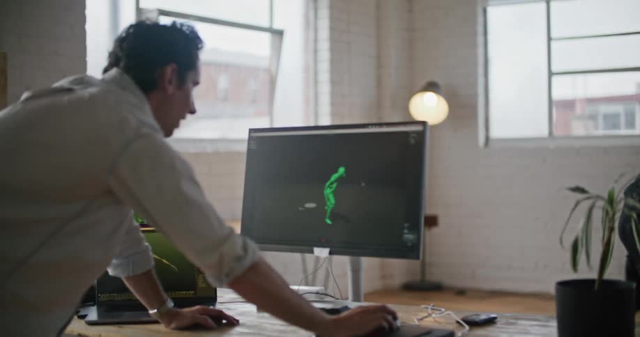 A man wearing interactive computer virtual reality devices is doing martial arts movements as another man watches him on a computer monitor