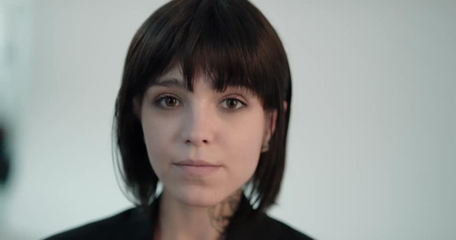 A woman with short black hair looks over to her side and then looks ahead and smiles