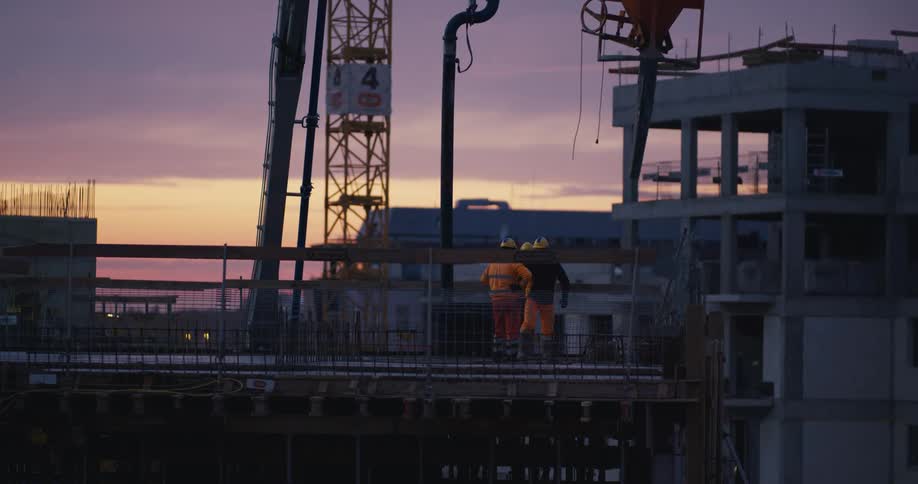 Three men are doing lightduty construction work as a crane lifts away a large bucket at dusk