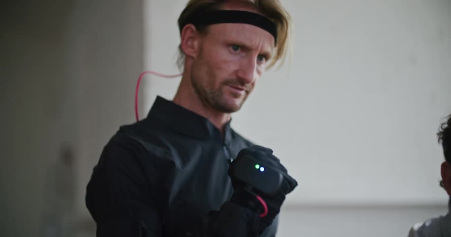 A man with an electrical device strapped to his hand squeezes his fingers as he talks with someone