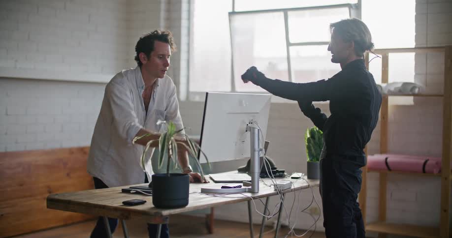 Man in white shirt gives instructions to another man wearing a futuristic motion capture black suit