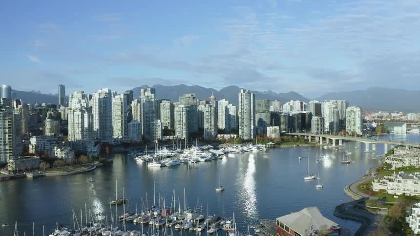 An aerial view of office buildings in Vancouver skyline on the shore with boats sailing in the water and cars driving across a bridge