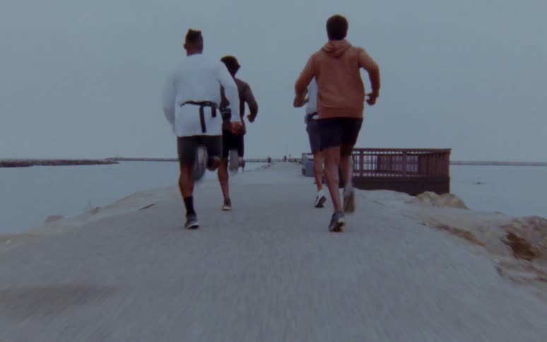 Group of men jogging over a road near the ocean