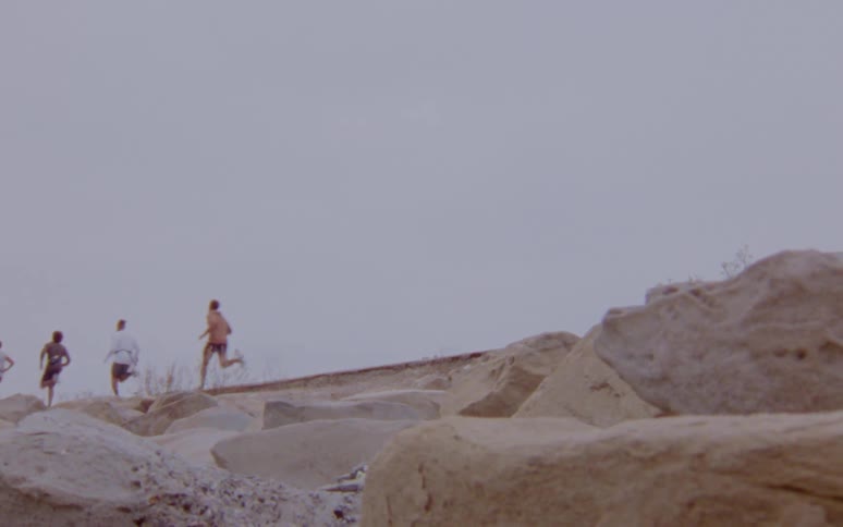 Group of men jogging on an elevated road over the rocks caught on vintage film