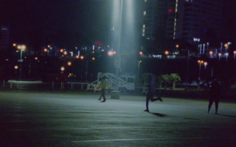 A person runs across a parking lot as another man stretches and two men walk and one gets in position to race