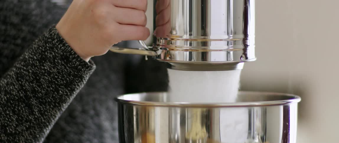 A person sifts flour into a metal bowl