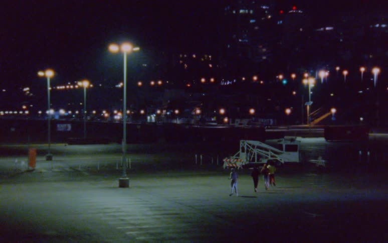 Group of four men jogging on a parking lot in the city at night caught on vintage film