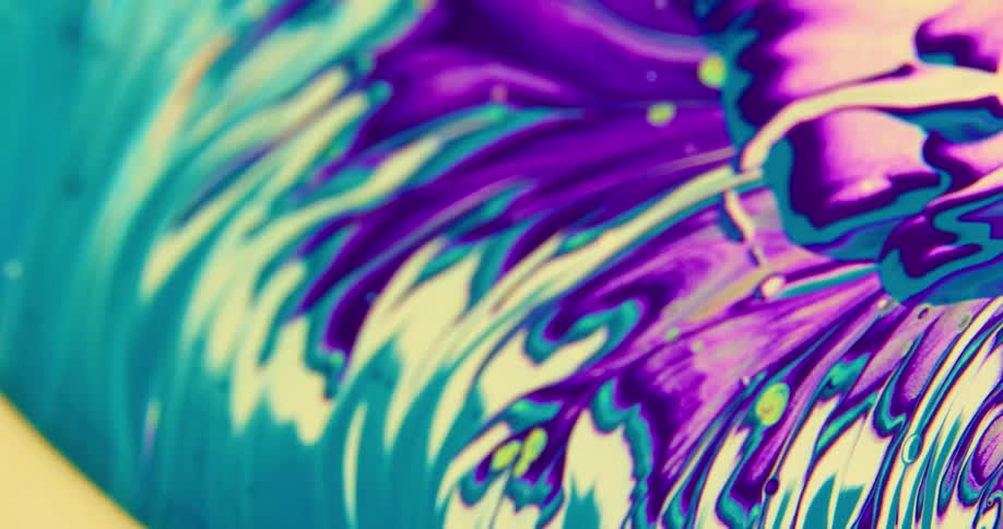 Camera spins over a surface covered with streaks and blobs of psychedelic white and blue liquid ink