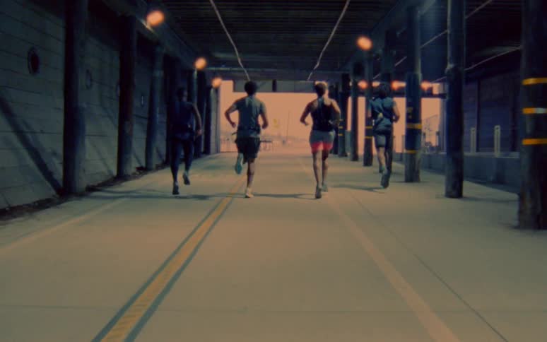 Four men run underneath bleachers in a stadium in tandem