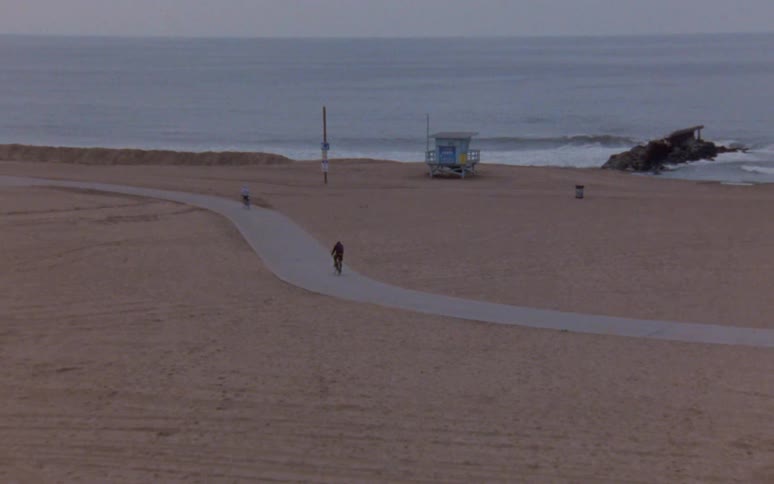 People driving bicycles on a road on the sand close to the beach next to the ocean caught on vintage film