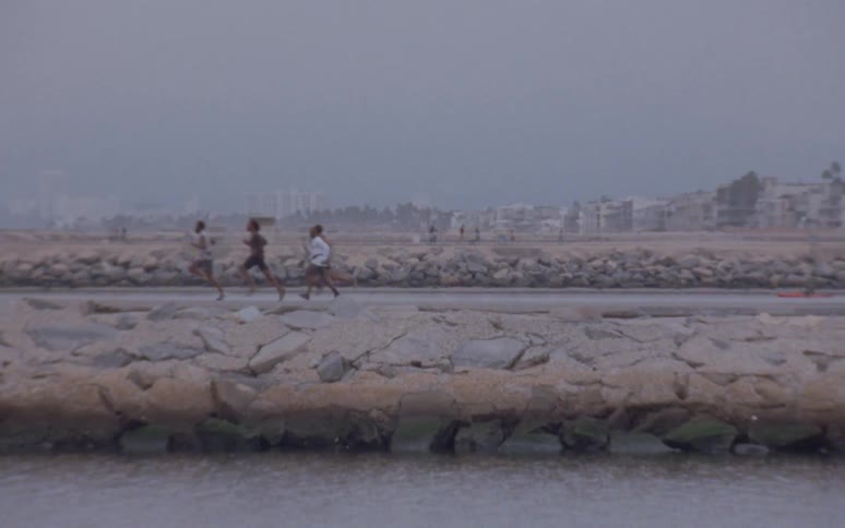 People walk toward town on foggy day as youths run along road close to water