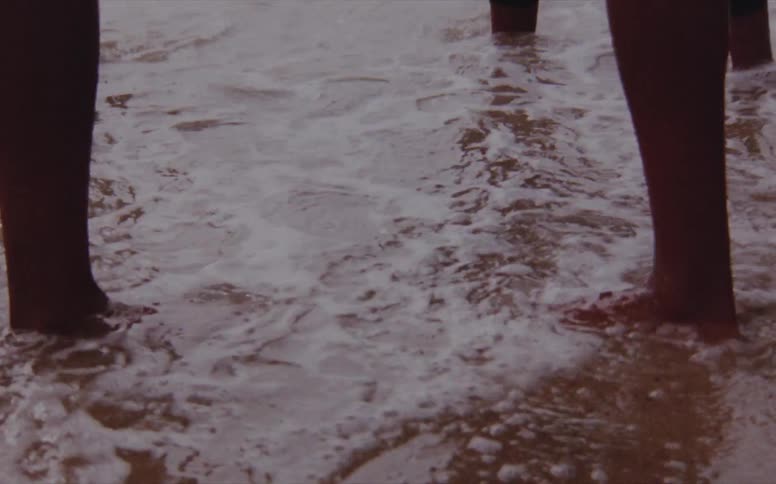 Three men stand on the shore as waves roll over their feet