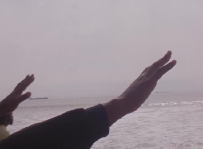 Man with hands extended on the beach close to the ocean caught on vintage film