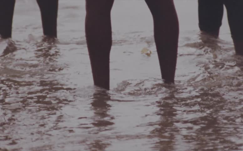 Three men stand in the ocean as waves ripple around their ankles