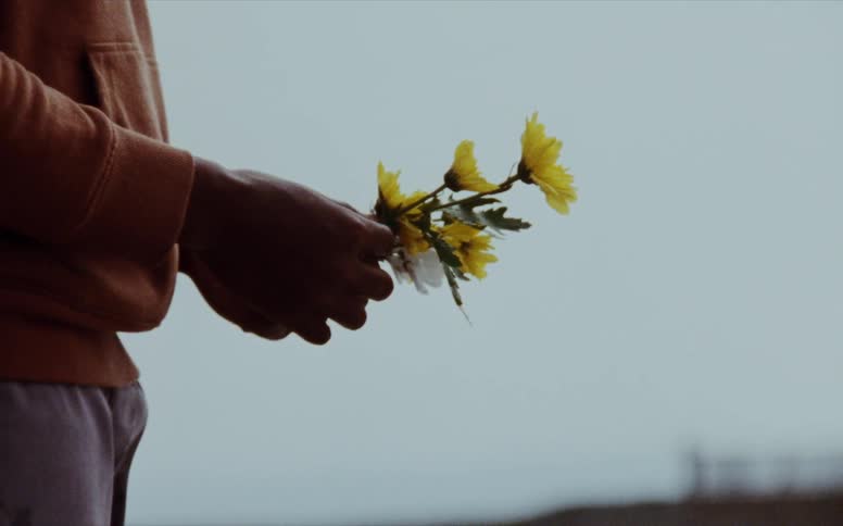 A man is standing on a beach holding yellow flowers on an overcast day