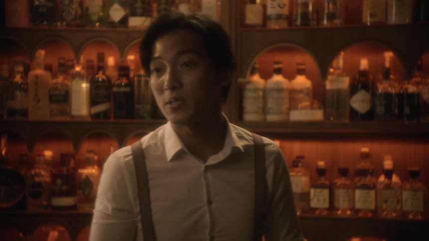 Young bartender wearing white shirt and suspenders handshakes and serves a client on a bar