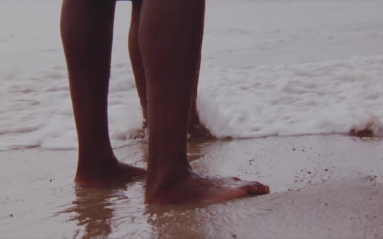 Sea wave breaks against the coast and legs of men standing on the beach
