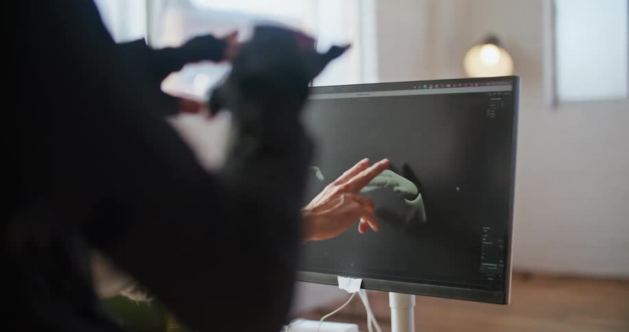 A man has virtual reality devices on his hands and his hand movements are seen on a computer monitor