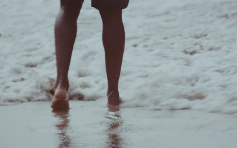 A man stands on the shore as waves rush over his feet