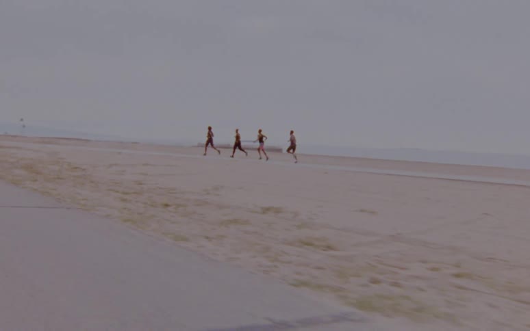 Four people are running across a beach