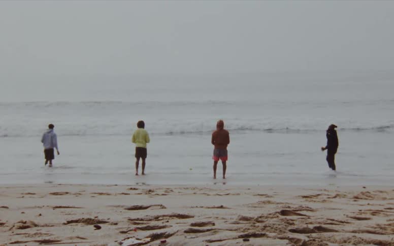Four men stand evenly spaced apart in the ocean