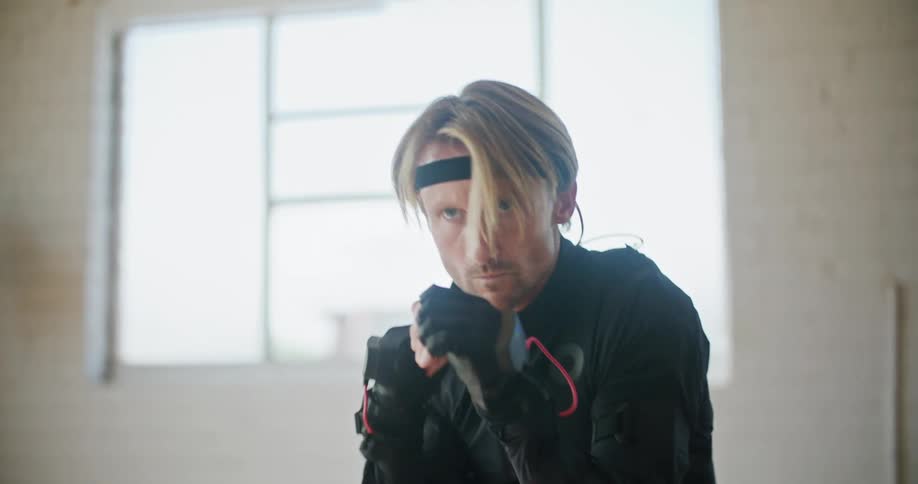 Man wearing a black motion capture suit moving into fighting poses inside a white room
