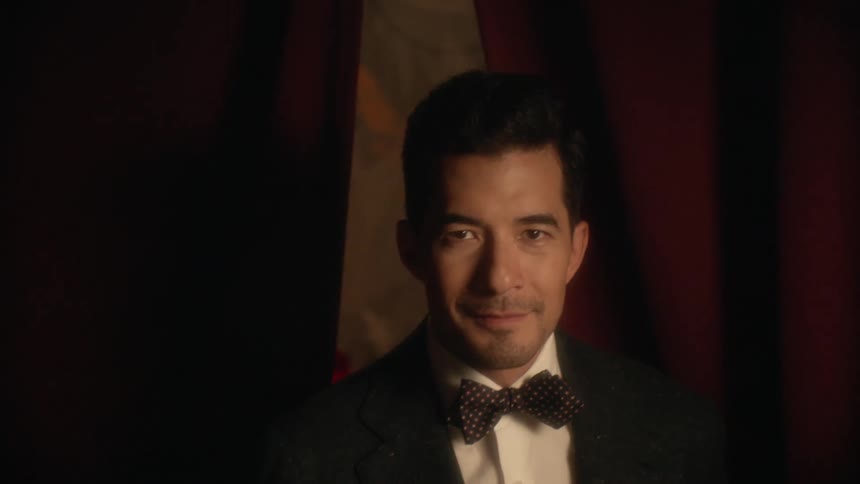 A man in a tuxedo walks out from behind a curtain