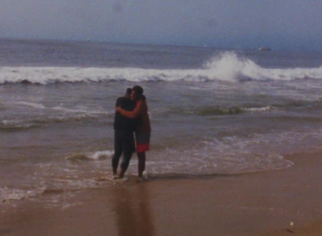 Two men hug as they stand on the beach near strong ocean waves