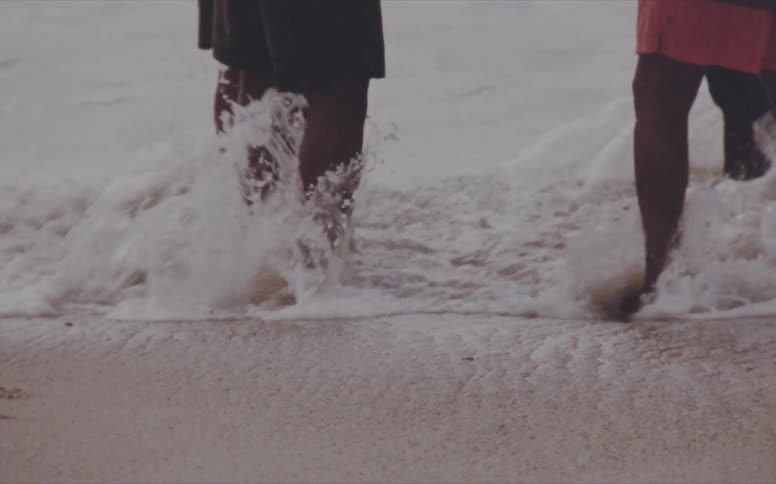 Four men stand on the shore together as waves splash up their legs