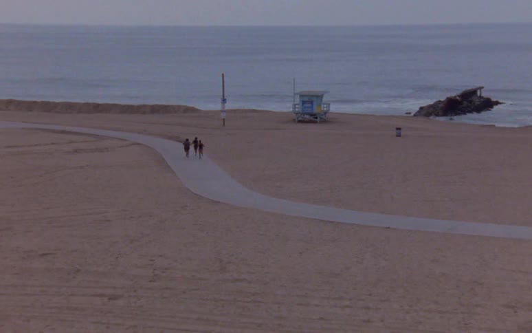 Two cyclists and four runners travel on the path at the beach next to the ocean