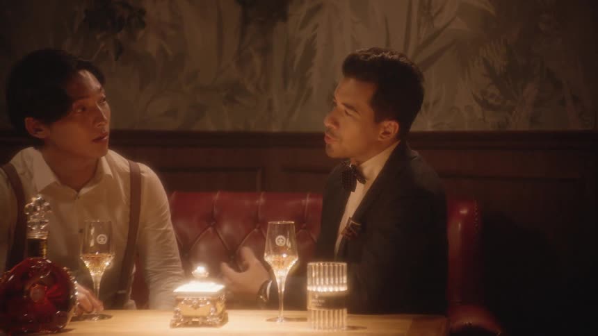 Man in a suit drinks wine while he talks with an asian man in a restaurant