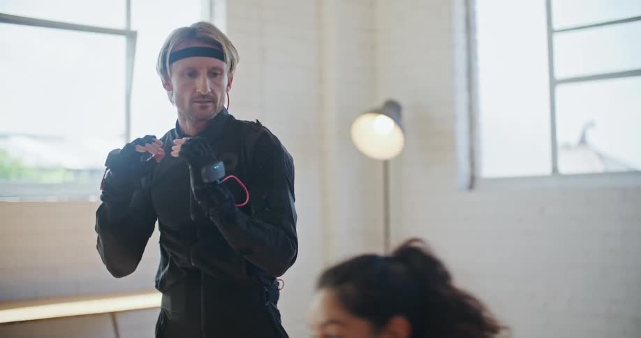 A man wearing virtual reality equipment laughs as a woman instructs him how to punch and move