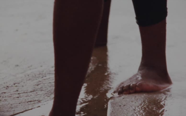 Barefoot men standing on the wet beach sand washed over by waves caught on vintage film