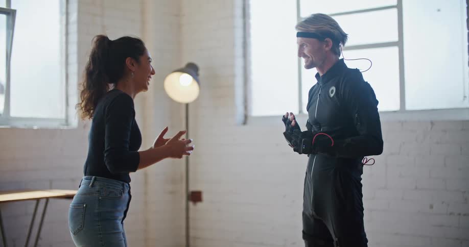 A man wearing interactive computer virtual reality devices is standing in a room near a woman he is having a conversation with