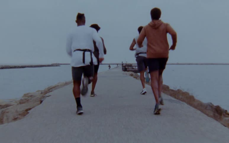 Four men are jogging on the coast of a beach