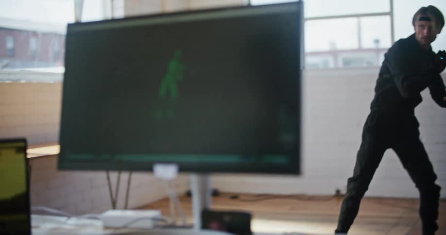Man wearing sensors moves through poses as another person sits in front of computer watching captured motions