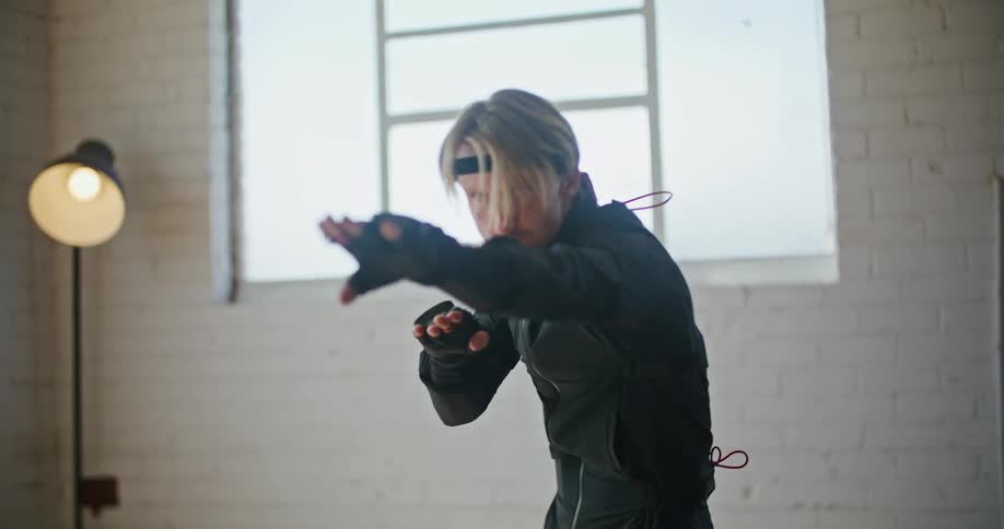 Man wearing a black motion capture suit moving into fighting poses inside a white room