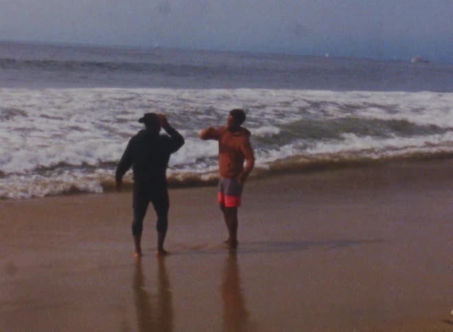 Two friends handshaking while standing on the sand of a beach next to the ocean caught on vintage film