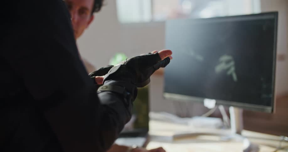 Man looks at a pair of hands wearing virtual reality gloves that are being held in front of a monitor
