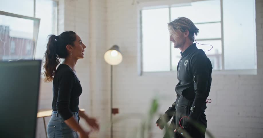 A man wearing virtual reality devices is speaking with a woman and moving his hands in the air and kicks