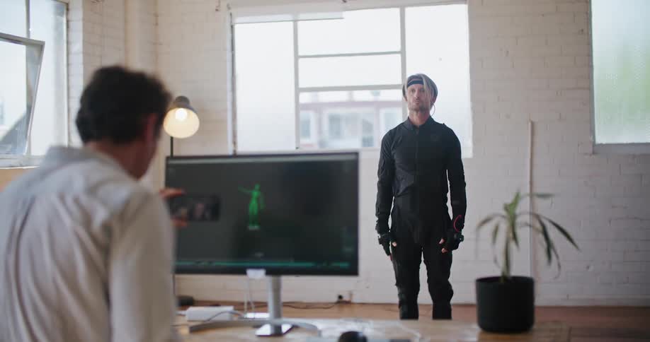 Man on a video call through a phone in front of an actor performing on a motion capture suit