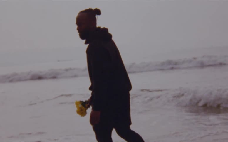 Man carrying a bouquet of wild flowers on the beach next to the ocean caught on vintage film
