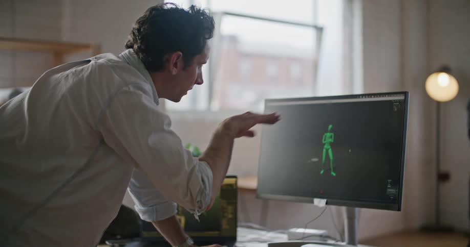A man wearing virtual reality devices movements are seen on a computer screen another man is watching