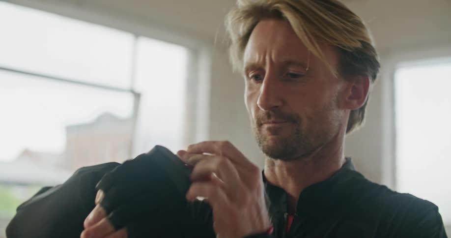 A man putting on fingerless gloves next to a sunny window