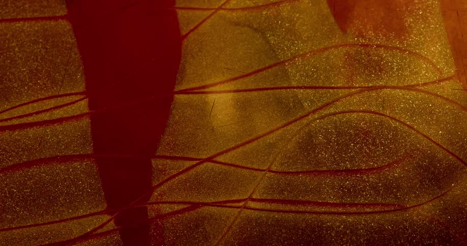 Wavy line appears on a surface covered in red and gold glittering liquid ink