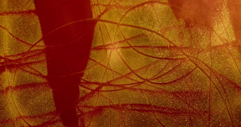 Wavy line appears on a surface covered in red and gold glittering liquid ink