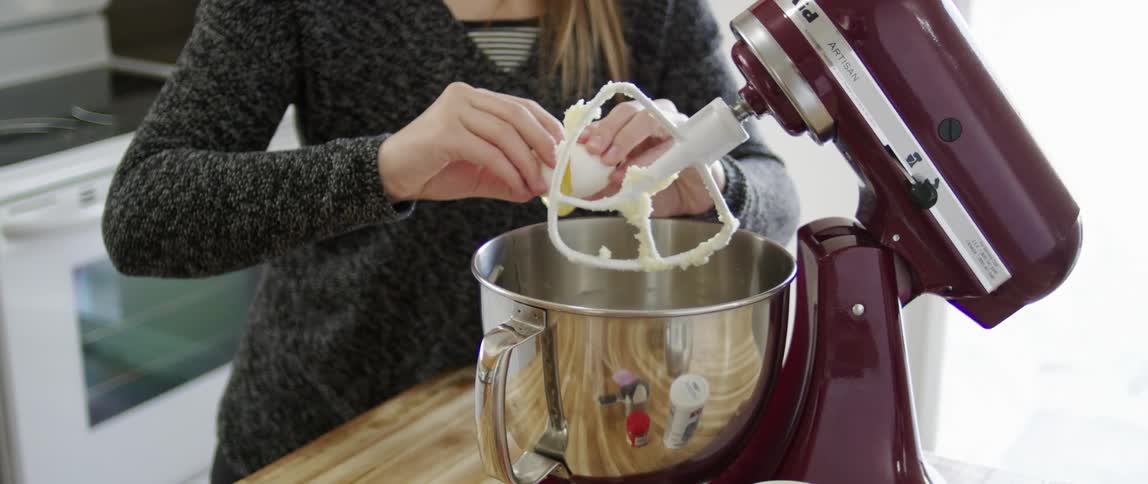 A woman breaks an egg into a mixer